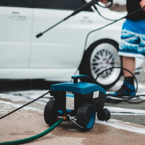 A person washing a white car with a pressure washer in outdoor setting, showcasing vehicle maintenance.